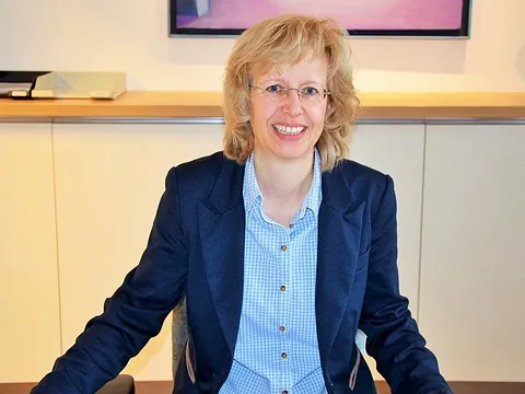 Lächelnde blonde Frau mit Brille im blauen Blazer.