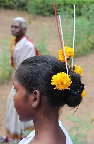 Junges Mädchen mit gelben Blumen und bunten Stäbchen in ihrem dunklen Haarknoten.