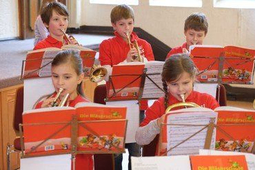 Kinder in roten Hemden spielen Blechblasinstrumente, lesen Noten.