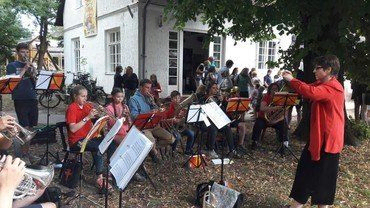 Jugendorchester spielt Blechblasinstrumente draußen mit Dirigentin.