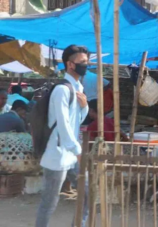 Person mit Gesichtsmaske und Rucksack auf einem Marktgelände.