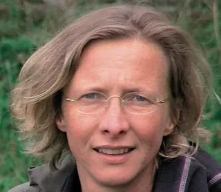 Frau mit kurzen, hellbraunen Haaren und Brille, lächelt leicht.